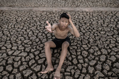 Portrait of shirtless boy sitting on cracked land