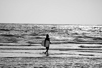 Rear view of man with surfboard on beach against clear sky