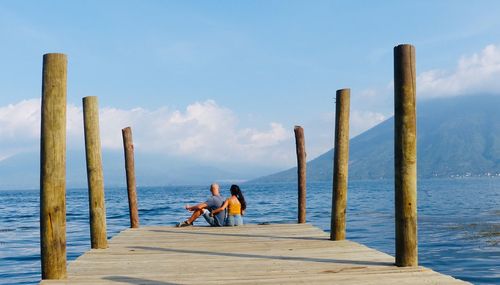 Men on wooden pier over sea against sky