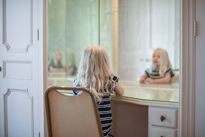 Rear view of girl sitting on chair in front of mirror