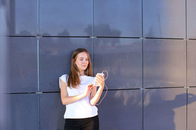 Portrait of young woman standing against wall