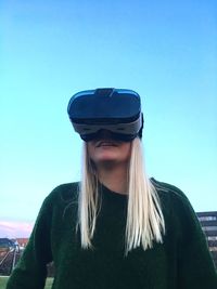 Low angle view of woman using virtual reality simulator against clear blue sky