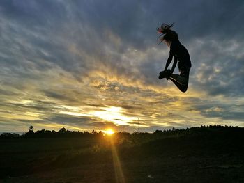 Low angle view of woman jumping on field against cloudy sky during sunset