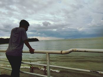 Full length of man standing on railing against sea
