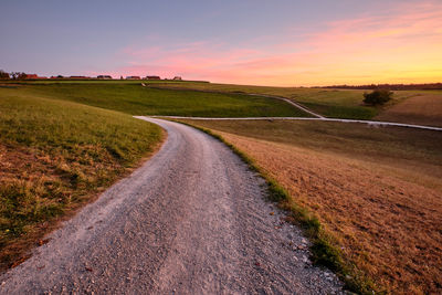 Road amidst field against sky during sunset