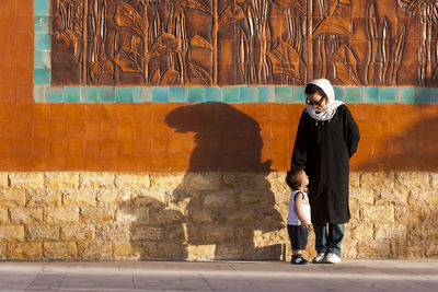 Mother with son standing on footpath against wall