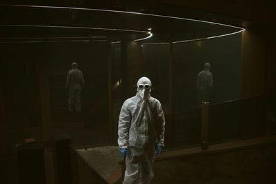 Man wearing protective suit standing against mirrors at hospital