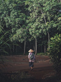 Rear view of woman walking on street amidst trees in forest