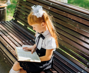 A child is sitting on a bench outside on a warm sunny day, and is returning to school. 