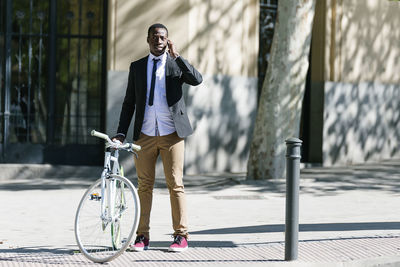 Businessman with bicycle talking on smart phone in city