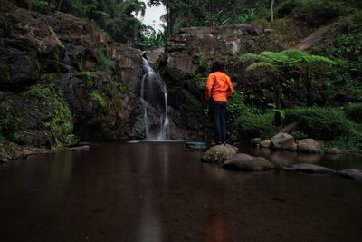 Man standing on rock against waterfall