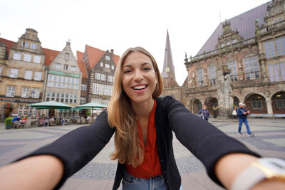 Pretty woman takes selfie photo in bremen market square with roland statue, bremen, germany