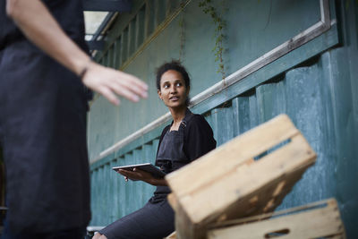 Female gardener holding digital tablet while friend gesturing by crates