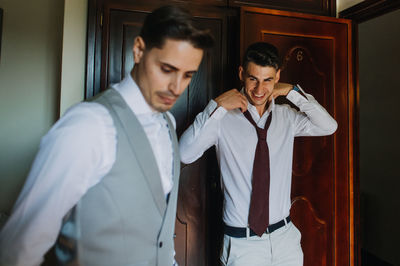 Groom and friend getting dressed at home