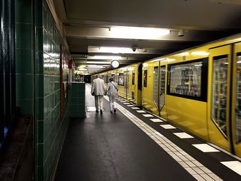 Rear view of man and woman walking by yellow train at subway platform