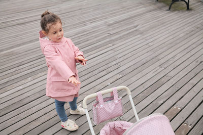 Young girl playing with her toy stroller on the boardwalk