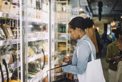 Side view of female customer examining broccoli at organic delicatessen