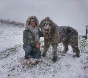 Woman with dog sitting on snow during snowing