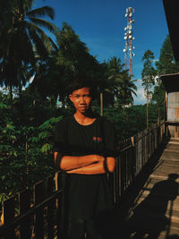 Portrait of smiling woman standing by railing against trees