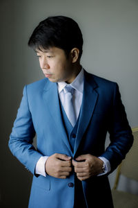 Young man looking away while standing against wall