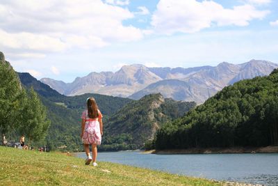 Rear view of young girl walking by lake against mountains