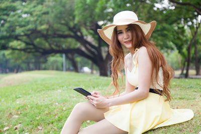 Close-up of young woman holding digital tablet while sitting on grass field