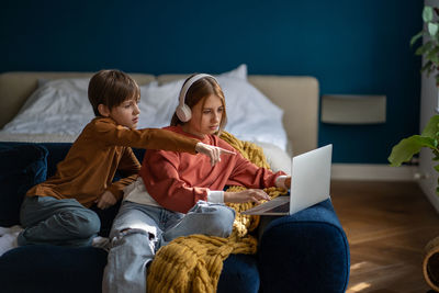 Teen girl and boy brother and sister watching movie together on laptop sitting on couch.