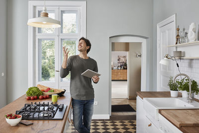 Happy man using tablet in kitchen looking at ceiling lamp