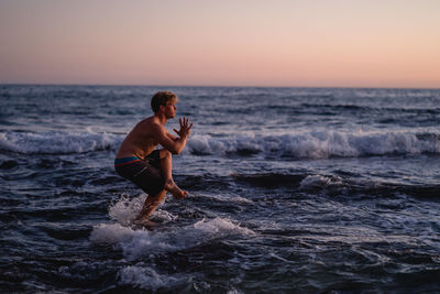 Full length of man exercising on shore at beach against clear sky