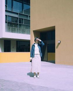 Young woman shielding eyes while standing against building