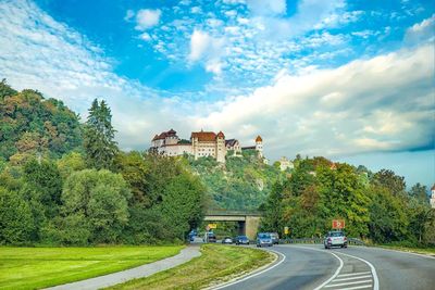 Road amidst trees and buildings against sky