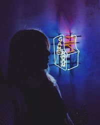 Side view of woman standing against illuminated wall