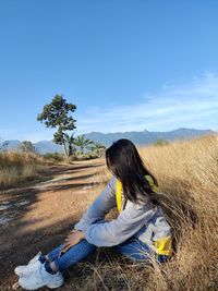 Woman sitting on field against sky