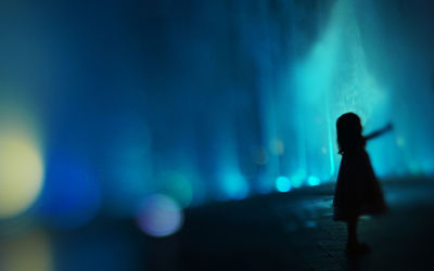 Silhouette girl standing by illuminated defocused light at night