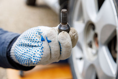 Mechanic hand in fabric glove holding car wheel bolt