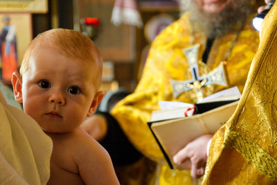 Close-up portrait of cute baby by priest in church