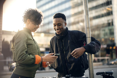 Teenage girl showing mobile phone to friend while standing by street in city