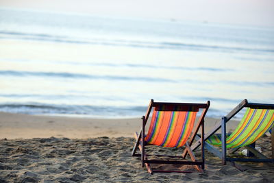 Deck chairs on beach against sky