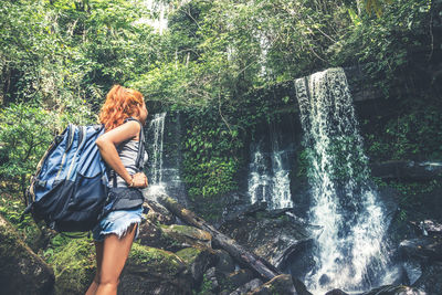 Low angle view of woman standing against waterfall in forest
