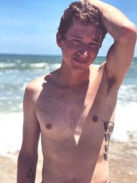 Midsection of shirtless man standing at beach against sky