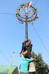 Low angle view of woman holding umbrella against clear blue sky