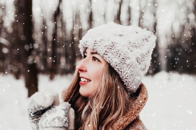 Beautiful woman in snowy winter woodland. girl wearing fluffy gloves, cap, coat. christmas forest