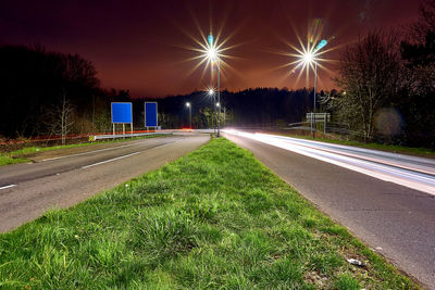 Empty road by illuminated street against sky at night
