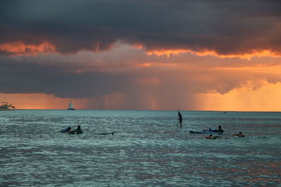 Silhouette people in sea against cloudy sky during sunset