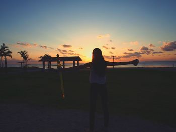 Rear view of silhouette boy playing on beach against sky during sunset