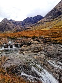 Scenic view of stream by mountains against sky