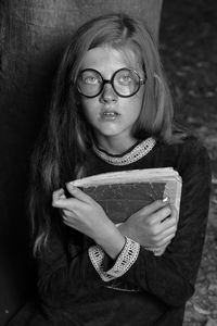 Portrait of girl in eyeglasses holding old book at home