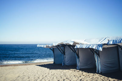 Huts at beach against clear blue sky