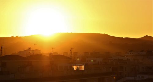 Silhouette buildings in city against orange sky