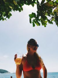 Young woman drinking glasses on beach against sky